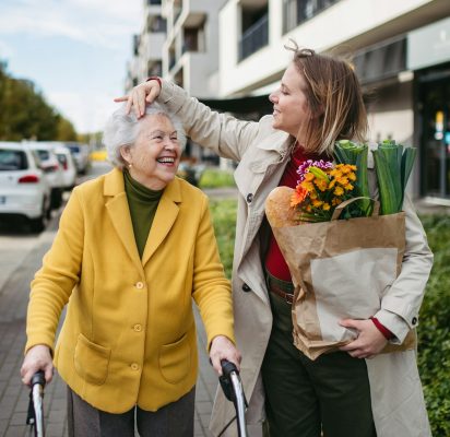 Mature granddaughter carrying grandmother's shopping bag. Senior woman and caregiver going to home